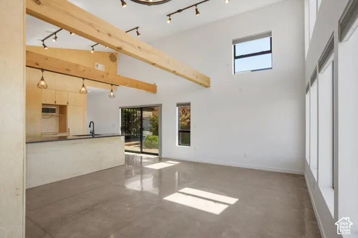 Vaulted ceilings with exposed wood beams, polished concrete flooring, extensive window placements, custom wood cabinetry, and a kitchen island with a dark countertop