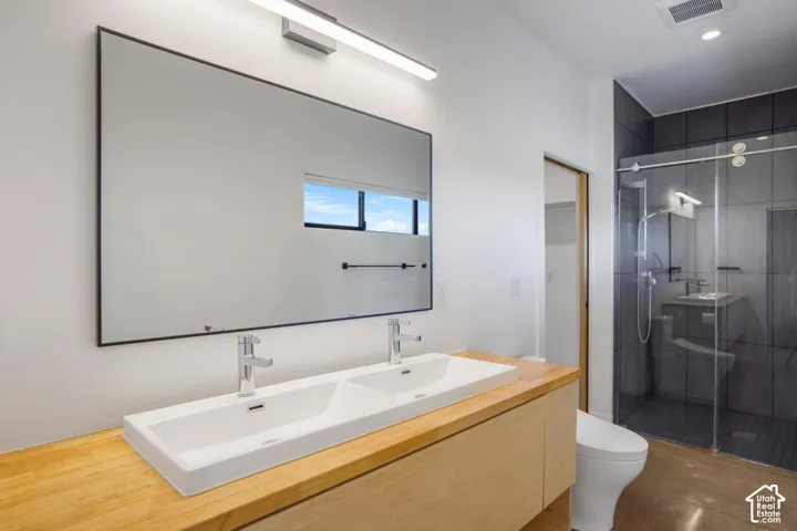 Dual basin vanity with wood-finish countertop, under-cabinet storage, and a large rectangular mirror with integrated lighting
