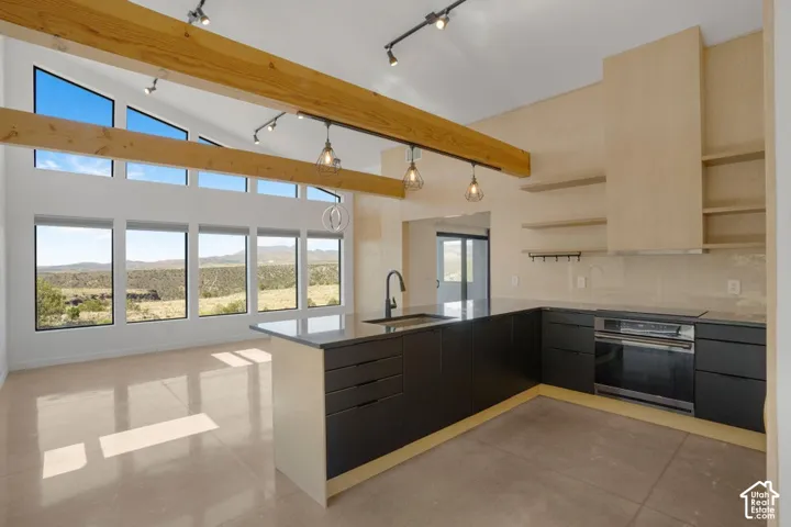Vaulted ceiling with exposed wood beams, expansive floor-to-ceiling windows, polished concrete flooring, contemporary kitchen with dark cabinetry, and integrated stainless steel appliances