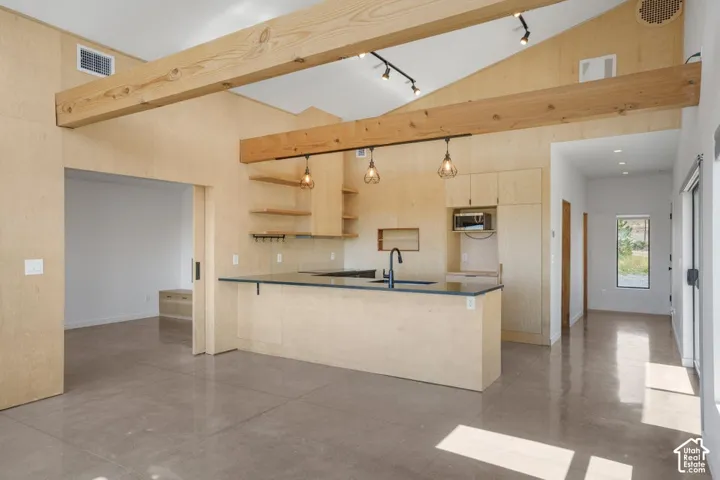 Vaulted ceiling with exposed wood beams, concrete flooring, built-in kitchen cabinetry, and track lighting