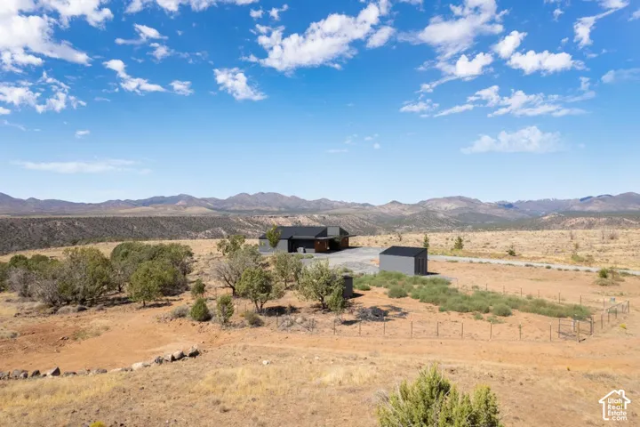 Expansive rural landscape featuring a contemporary residence with a dark exterior, a detached storage shed, and mature trees on the property