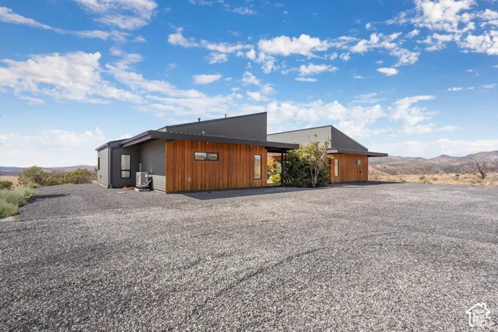 Modern architectural design featuring wood-clad and gray siding, a dark sloped roof, and a gravel driveway