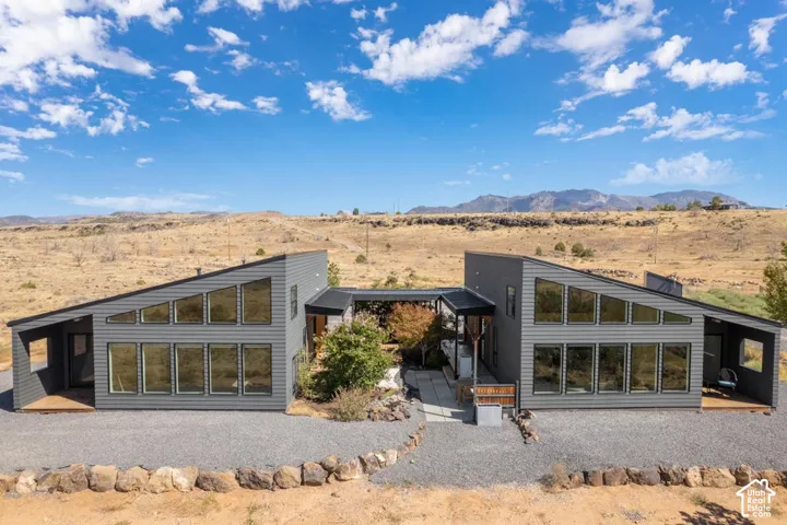 Contemporary split-level residence featuring a dark gray exterior, multiple large windows, and a gravel driveway
