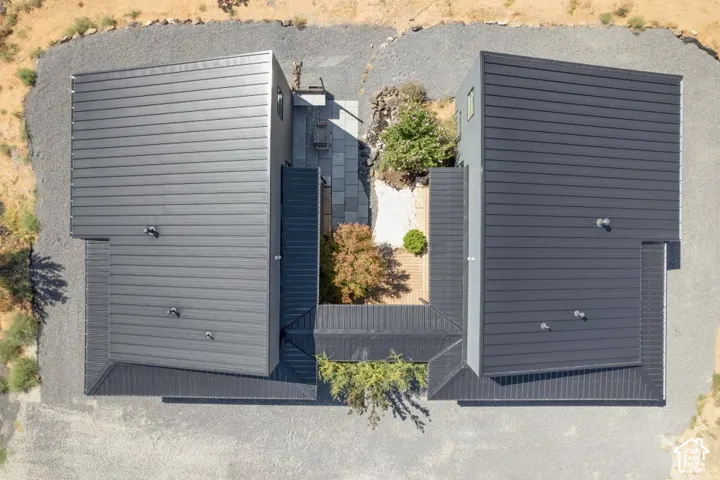 Dual modern structures featuring dark metal roofs, gravel landscaping, a central paver patio, and integrated decking