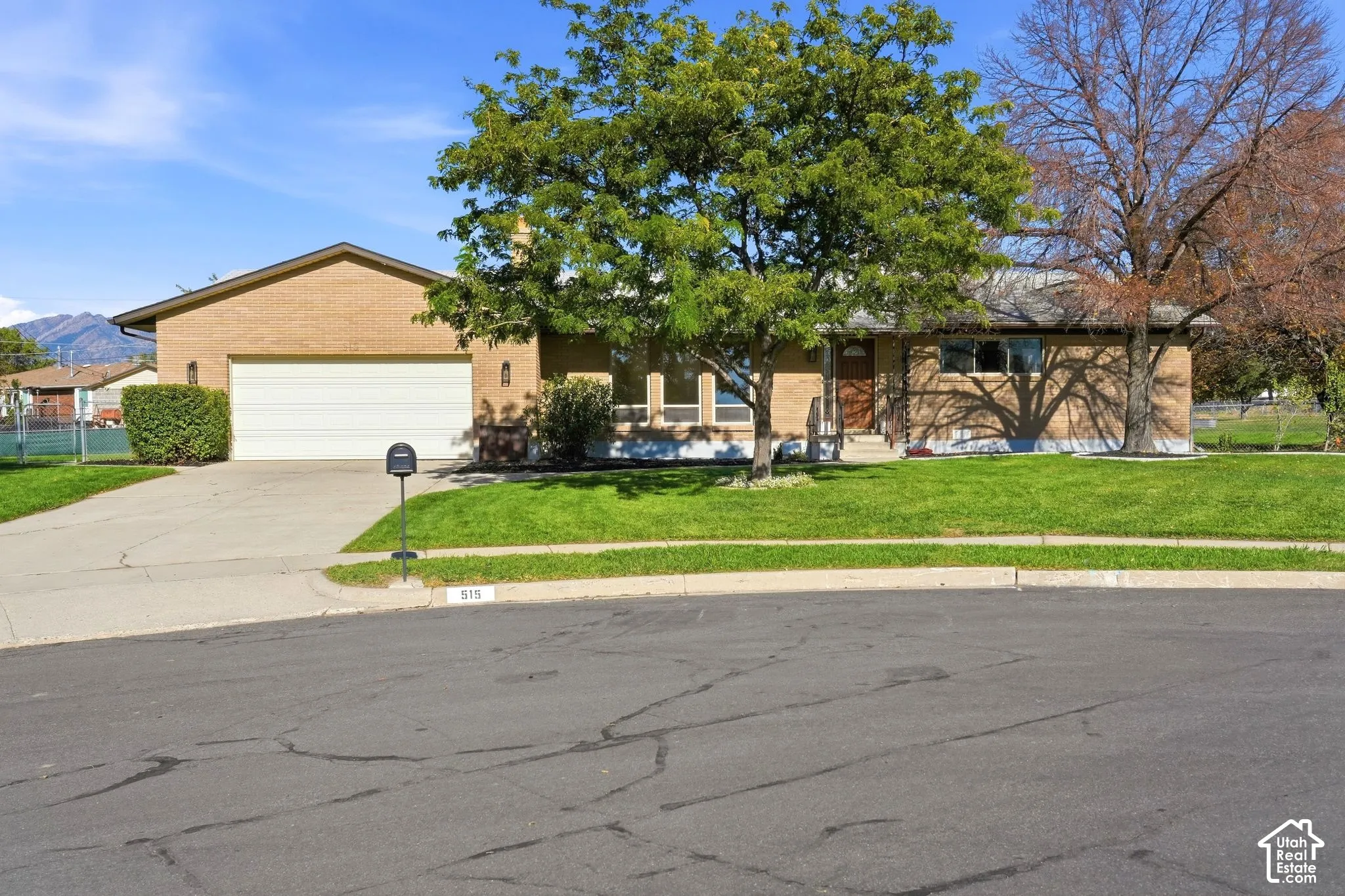Brick exterior home with an attached two-car garage, mature front yard tree, concrete driveway, and front lawn