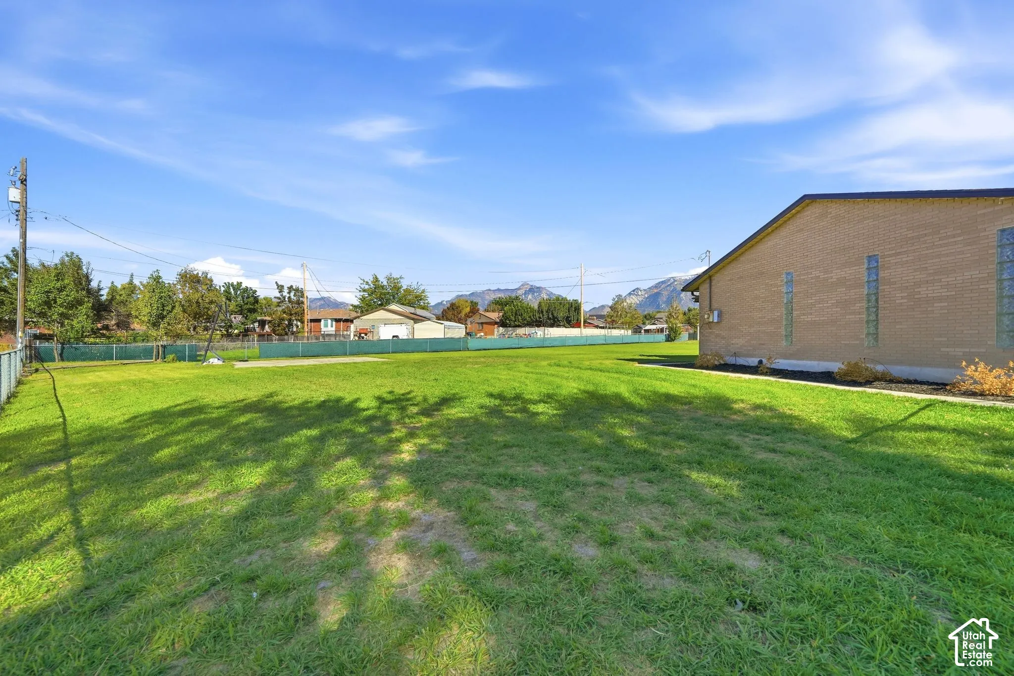 Expansive grass lawn with a chain-link fence, brick exterior, and mountain backdrop