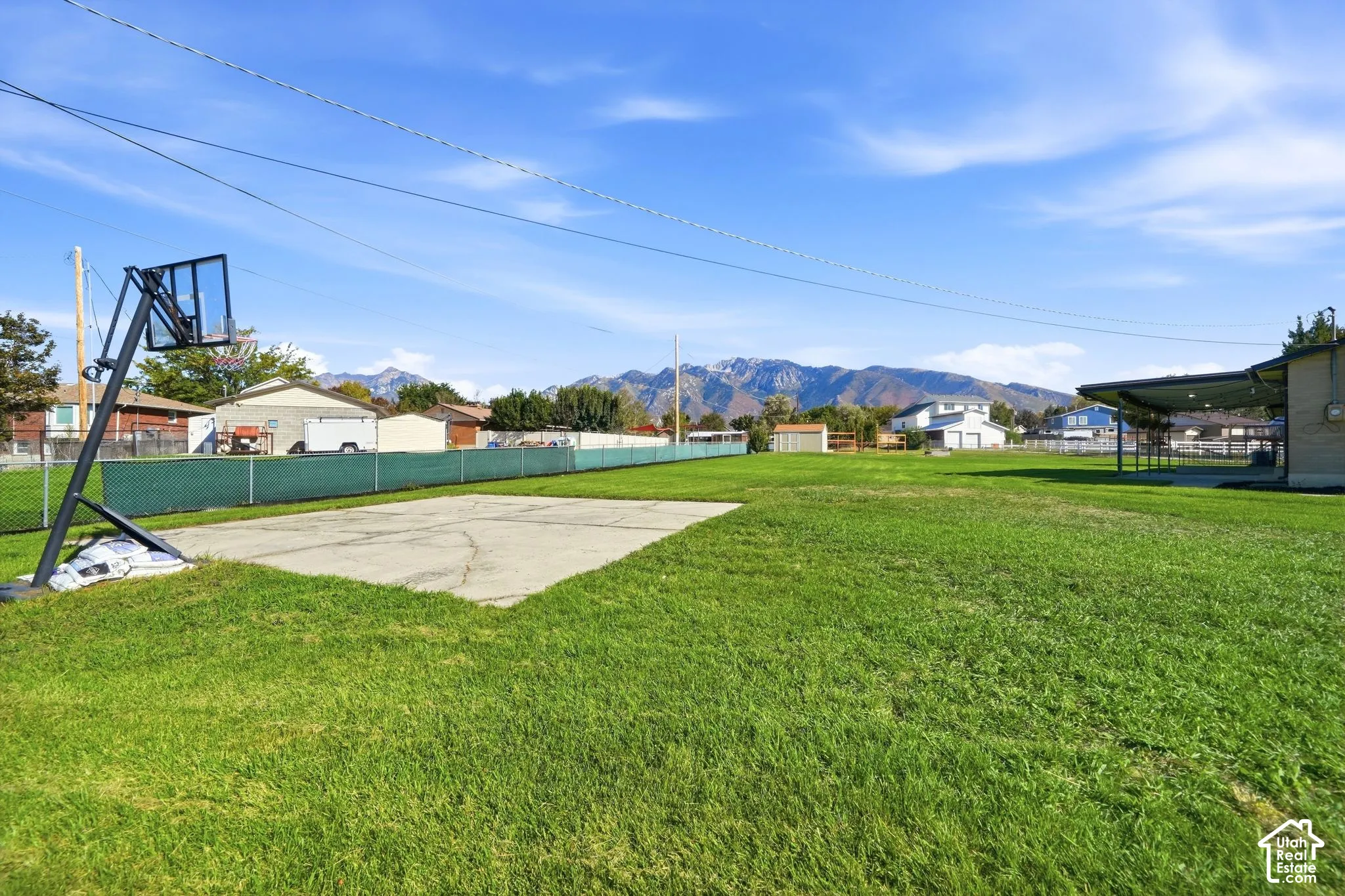Expansive grassy yard with mountain backdrop, concrete pad, and covered patio structure