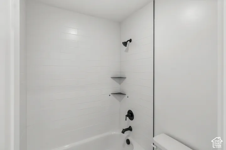 Bathtub shower with white subway tile surround, matte black fixtures, and two corner storage shelves