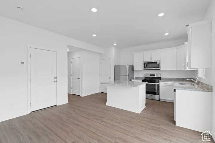 Modern kitchen featuring white cabinetry, stainless steel appliances, speckled countertops, a central island, and wood-finish flooring