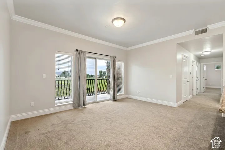 Neutral tone wall paint, crown molding, sliding glass door to a balcony, and carpet flooring