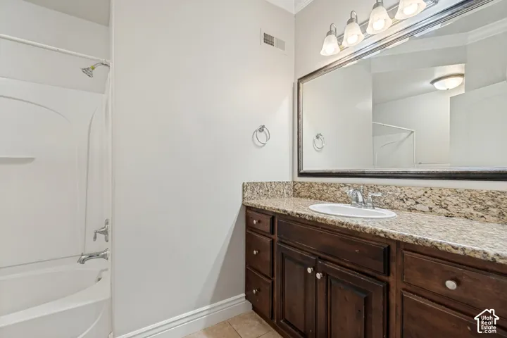 Tub-shower combination with a bright white surround, a dark wood-finish vanity with ample storage, a light-toned speckled countertop, and a large framed mirror with overhead lighting