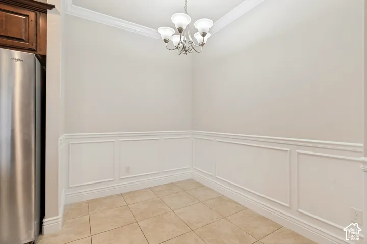 Tile flooring, decorative wainscoting, crown molding, and a built-in chandelier