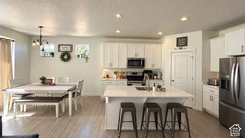 Open-concept kitchen and dining area featuring light wood-finish flooring, recessed lighting, and white cabinetry