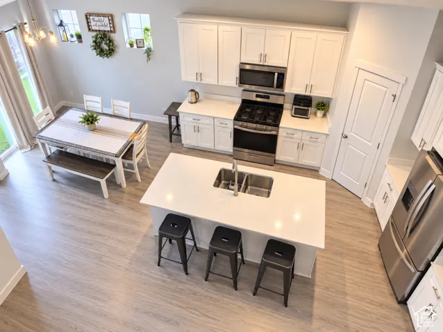 White cabinetry, stainless steel appliances, central island with seating, pendant lighting, and wood-finish flooring