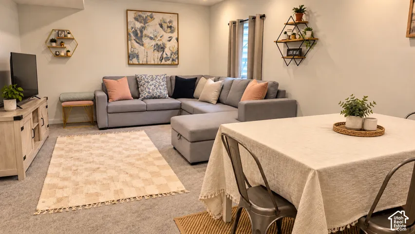 Carpeted living area featuring a built-in shelving unit, a window with curtain rods, and a dining area with metal chairs