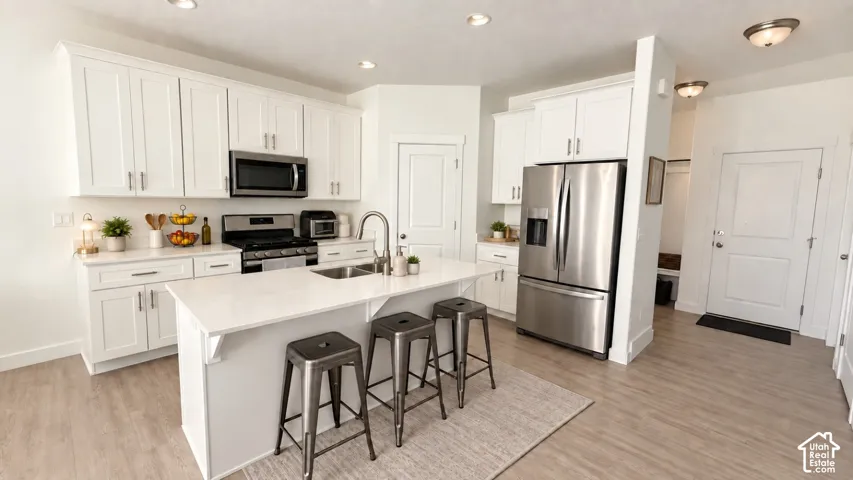 White shaker cabinetry, stainless steel appliances, central kitchen island with undermount sink, quartz countertops, and wood-finish flooring