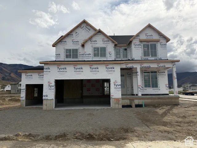 Two-story residential construction featuring a multi-gabled roofline, three-car garage, covered front porch, and mountain backdrop