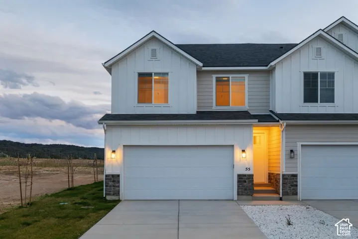 Two-story exterior featuring white board-and-batten siding, horizontal lap siding accents, stone veneer foundation detailing, and an attached two-car garage