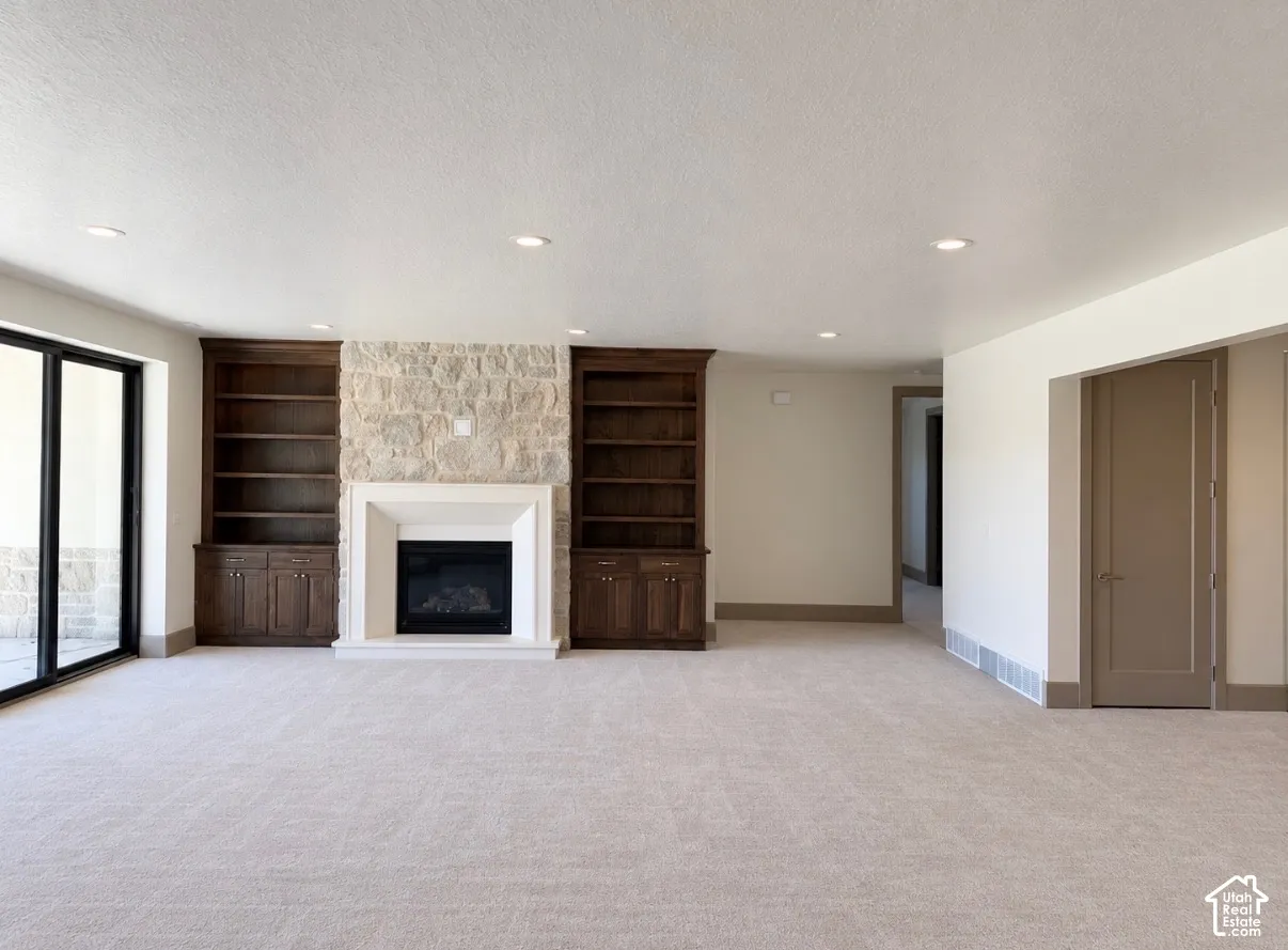 Spacious room featuring a stone fireplace with a light-toned surround, built-in dark wood cabinetry, recessed lighting, and large sliding glass doors