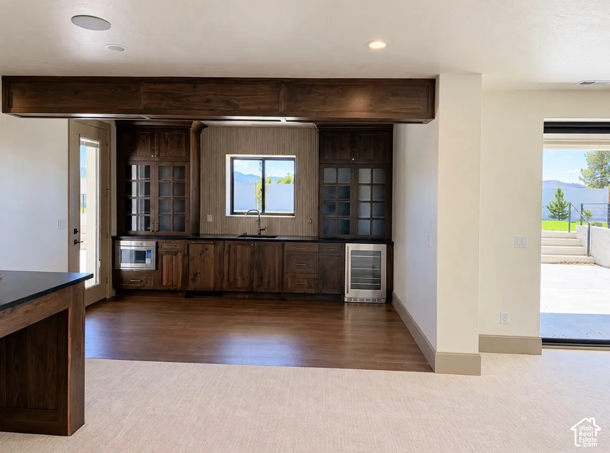 Built-in bar with wood cabinetry, dark countertops, an integrated microwave, and a beverage cooler