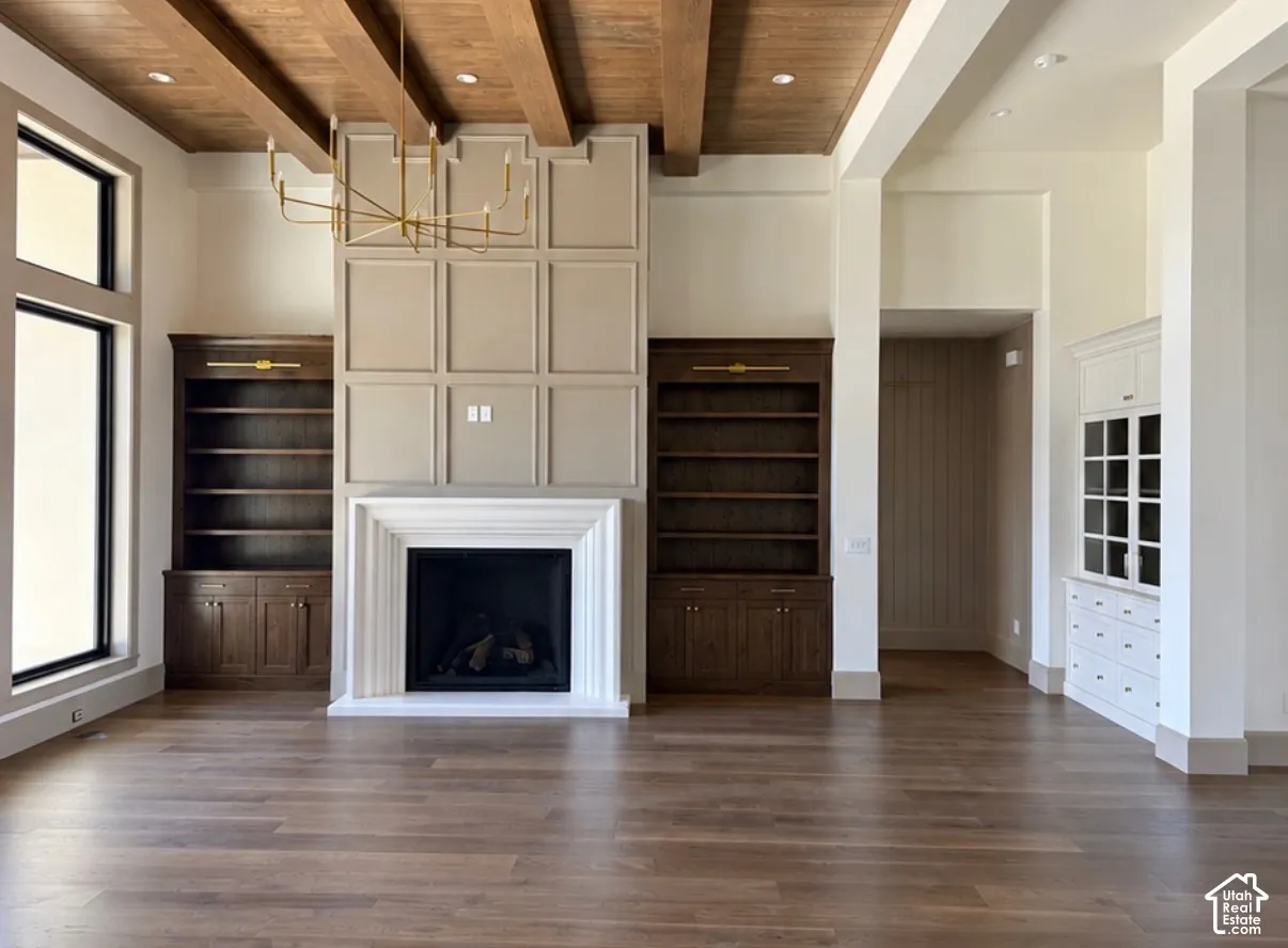 Wood-finish flooring, exposed wood beams, a fireplace with a detailed mantel, built-in dark wood cabinetry, and white built-in cabinetry with glass doors