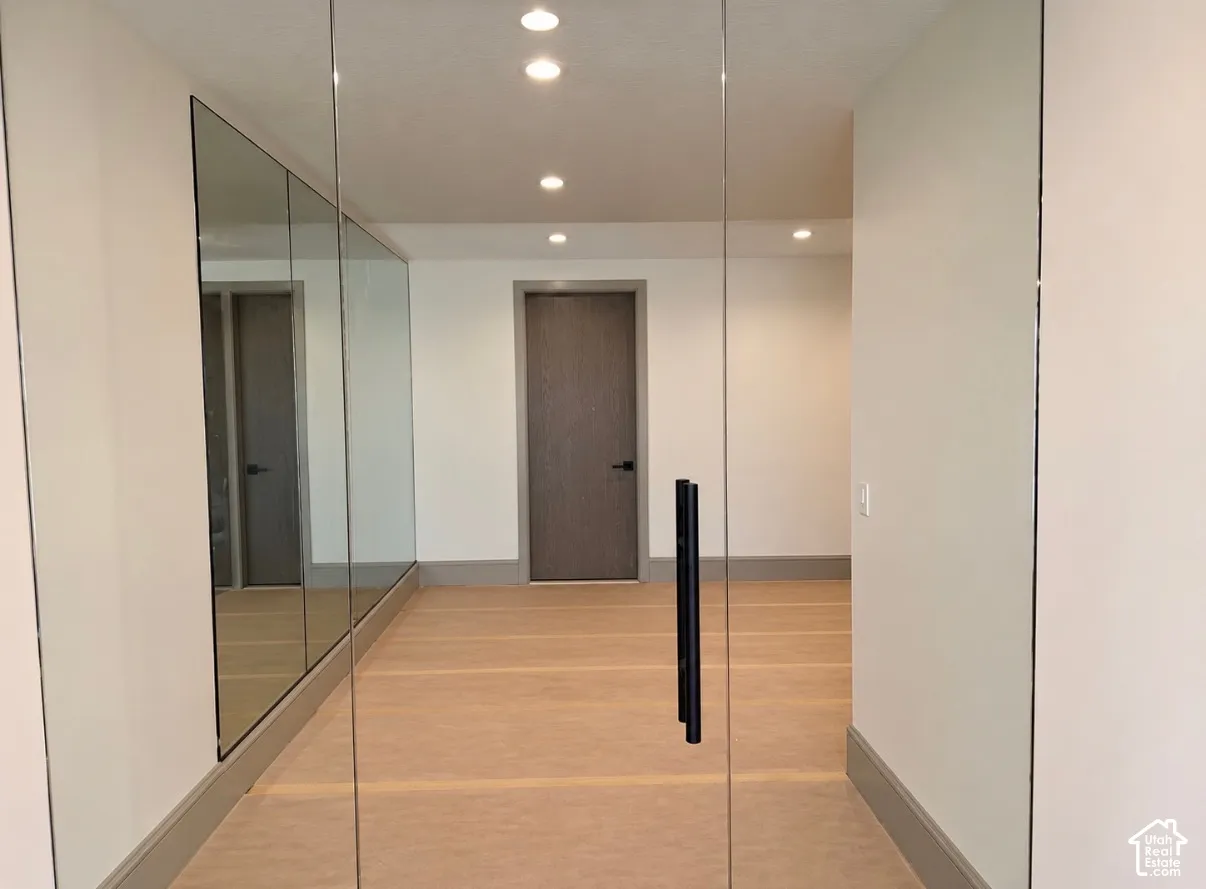Mirrored wall panels, recessed ceiling lighting, light wood-finish flooring, and a dark wood-finish door with black hardware