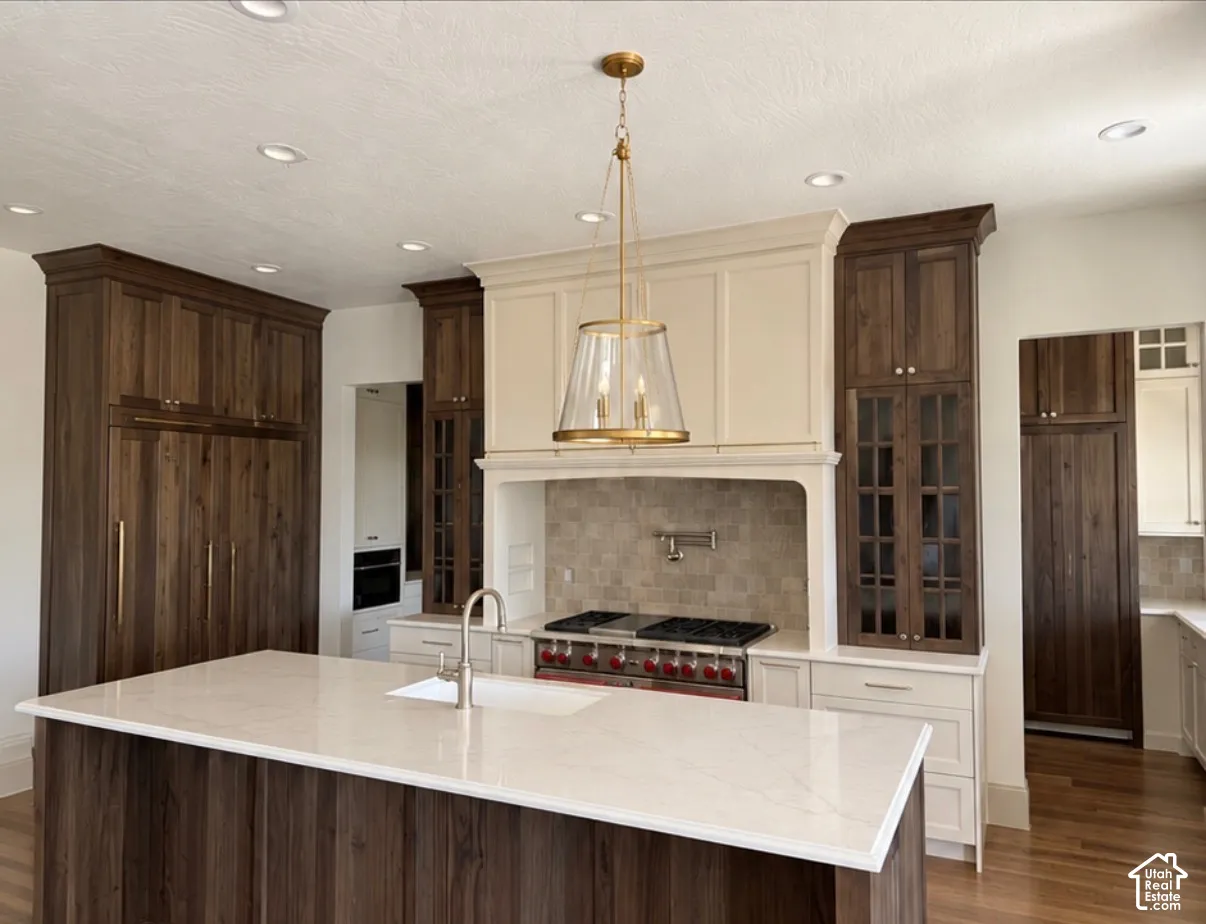 Spacious kitchen featuring an expansive island with a white countertop, rich wood-finish cabinetry, a tiled backsplash, and recessed lighting