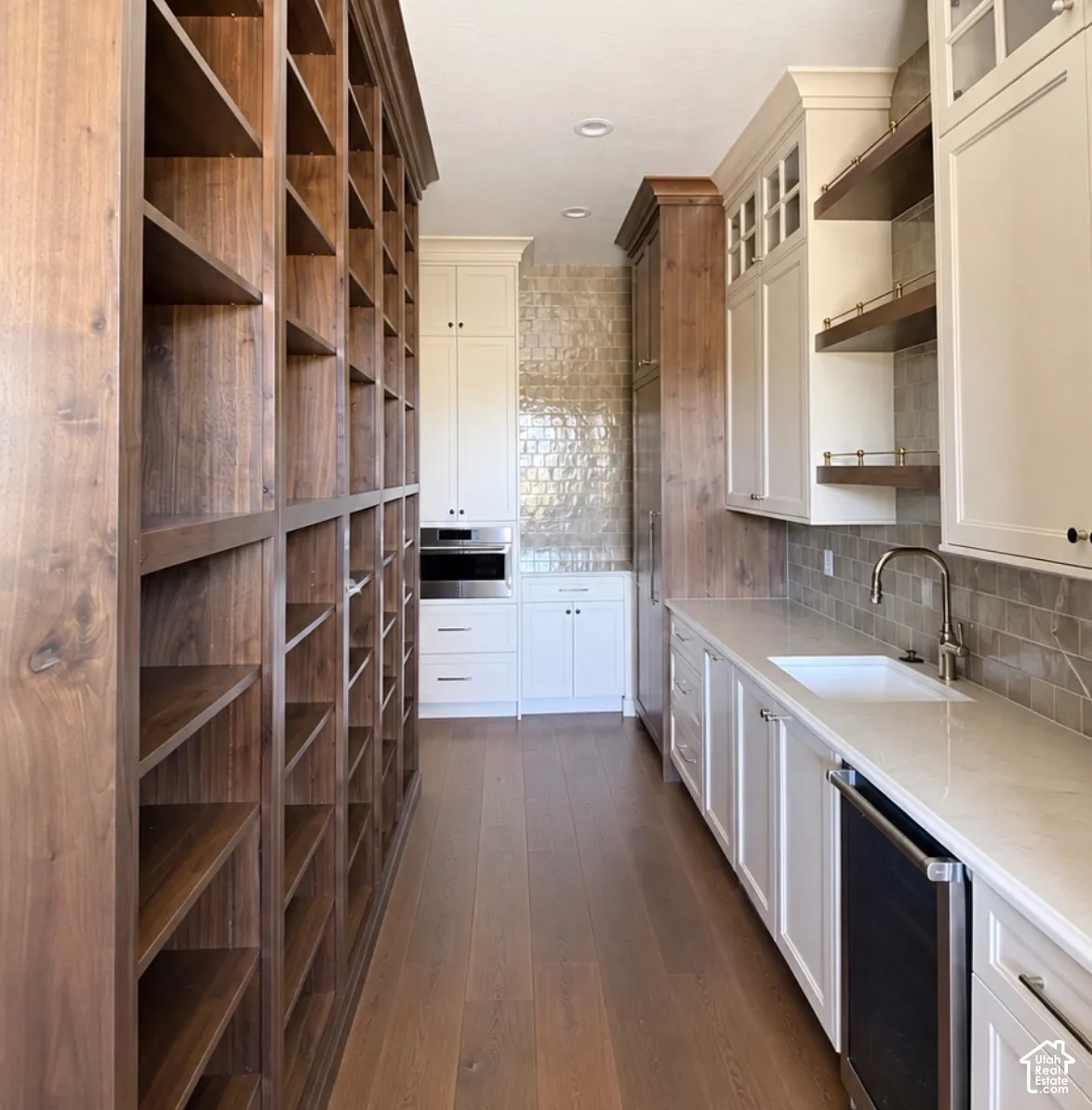 Extensive built-in wood shelving, wood-finish flooring, white cabinetry, integrated stainless steel appliances, and a polished chrome faucet