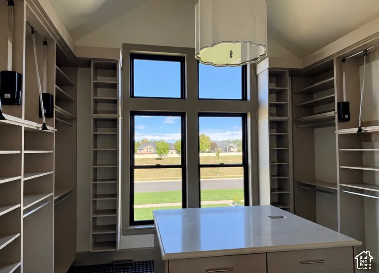 Built-in shelving, center island with solid surface countertop, vaulted ceiling, large multi-pane window, and integrated lighting fixture