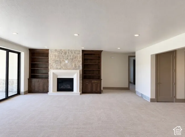 Spacious room featuring a stone fireplace with a light-toned surround, built-in dark wood cabinetry, recessed lighting, and large sliding glass doors