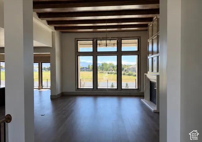 Vaulted ceiling with exposed wood beams, expansive floor-to-ceiling windows, wood-finish flooring, built-in shelving, and a prominent fireplace with a detailed mantel