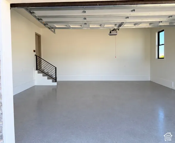 Polished concrete flooring, interior staircase with metal railing, single window, interior door, and garage door mechanism