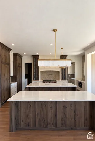 Kitchen featuring two large islands with white countertops, wood-finish flooring, recessed lighting, and a decorative linear chandelier