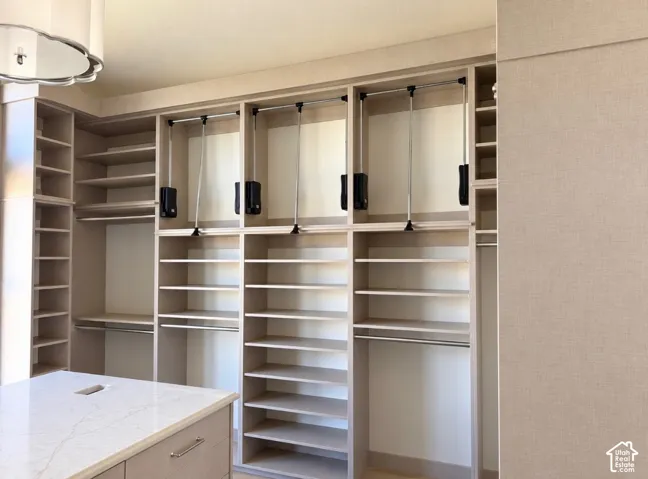 Custom closet system with varied shelving, multiple hanging rods, three pull-down rods, and a central island with a light-colored countertop
