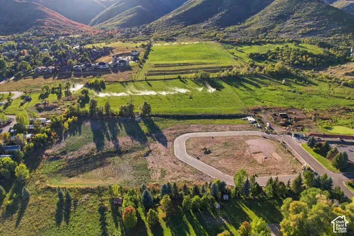 Undeveloped land parcel with paved access roads, surrounded by natural green spaces and distant mountainous terrain
