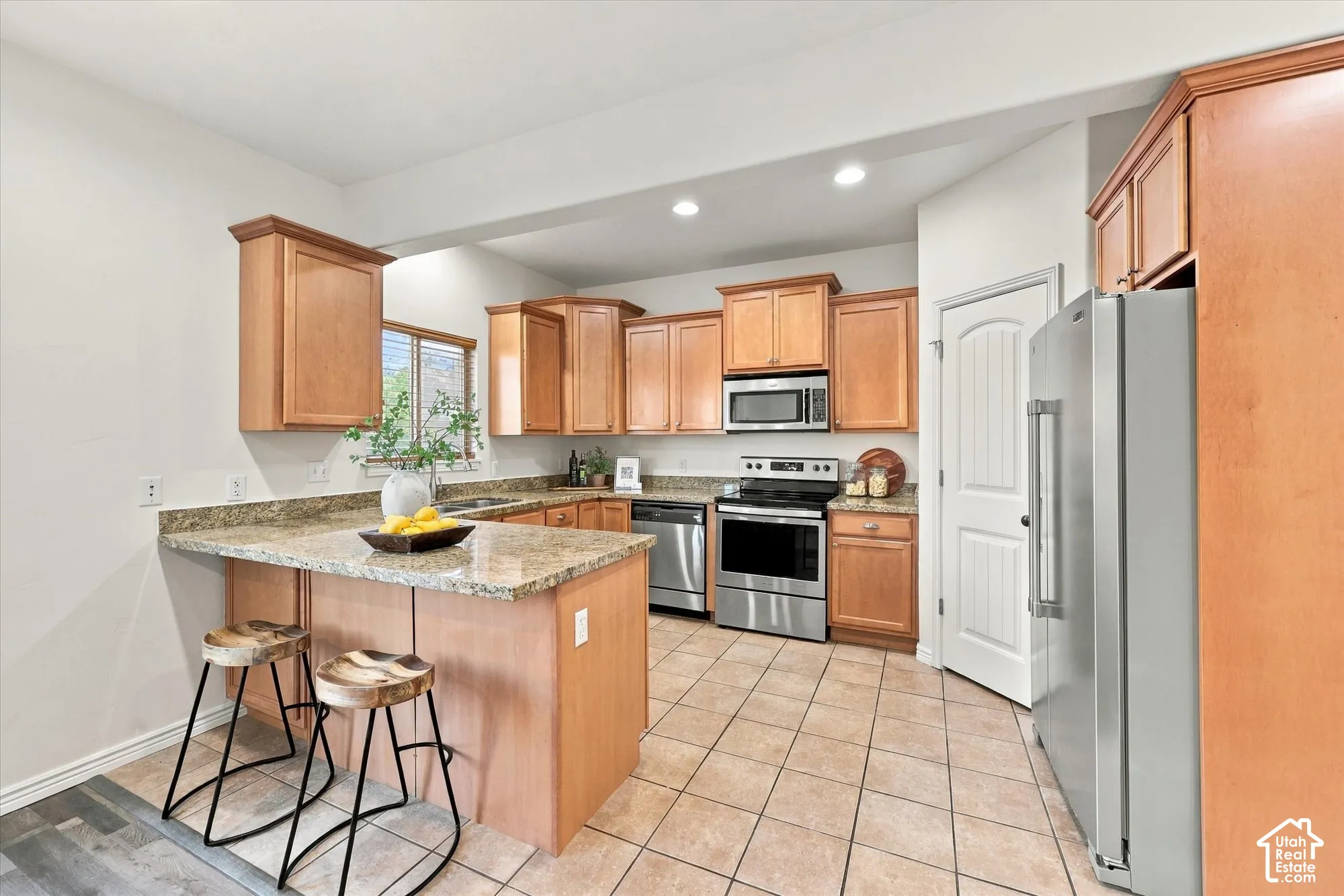 Kitchen featuring natural wood cabinetry, light-toned granite countertops, stainless steel appliances, and tile flooring