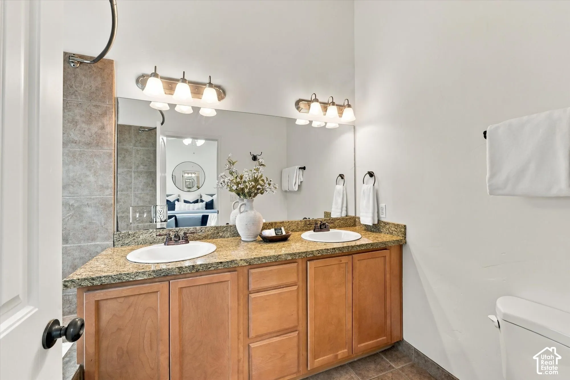 Dual vanity with integrated sinks, granite countertop, wood-finish cabinetry, and brushed nickel light fixtures