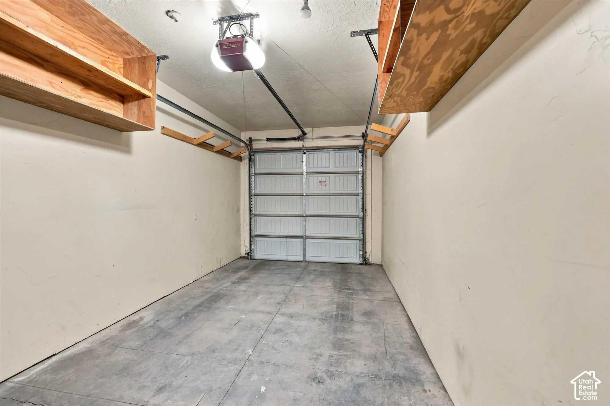 Garage with concrete flooring, overhead garage door, automatic garage door opener, and integrated wooden shelving