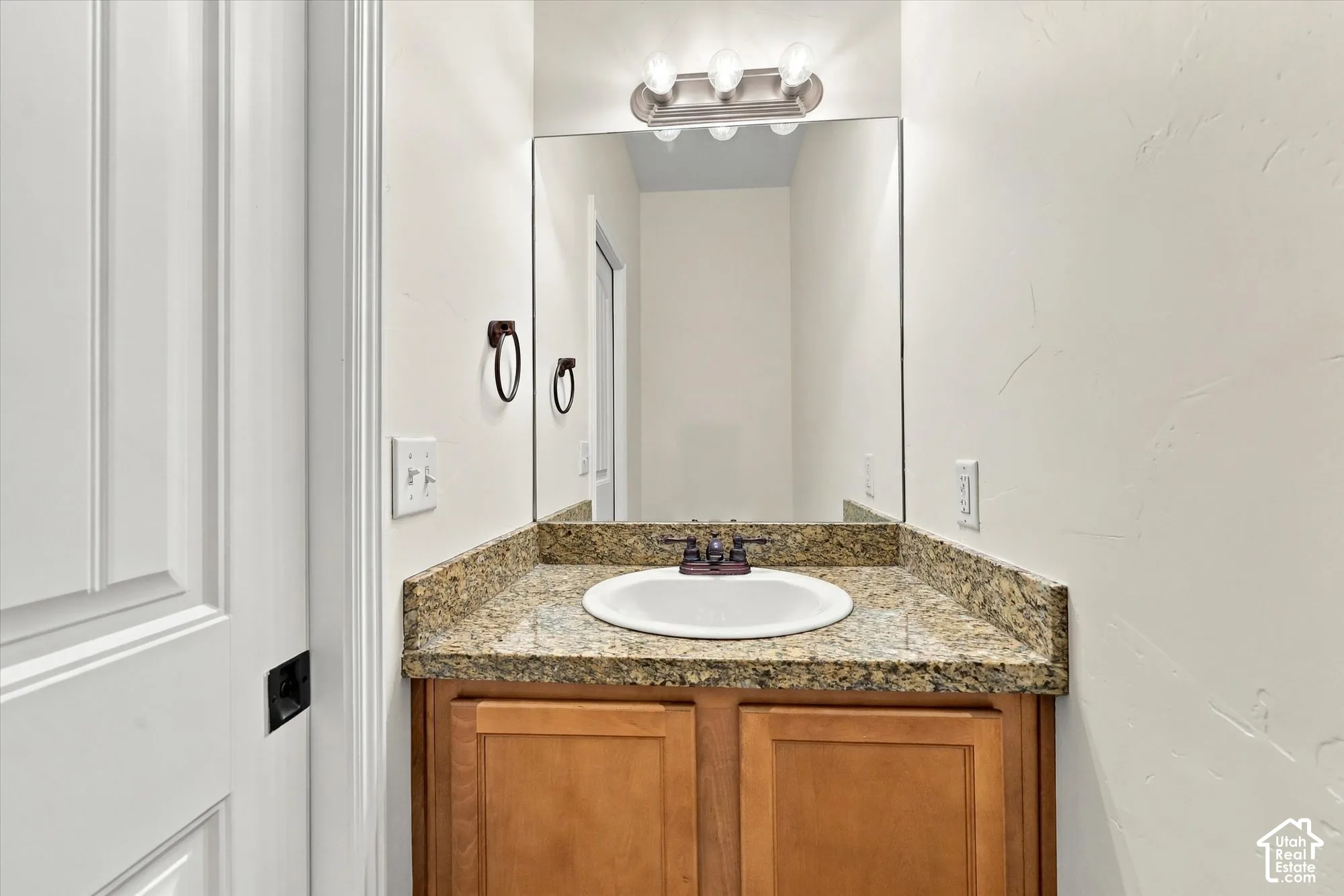Main level half-bath with light wood-finish vanity with cabinet storage, drop-in sink with bronze-finish faucet, and a wall-mounted mirror