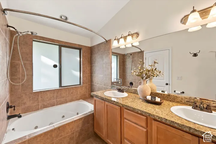 Jetted soaking tub with tile surround, frosted sliding window, dual vanity with granite-finish countertop, and integrated sinks
