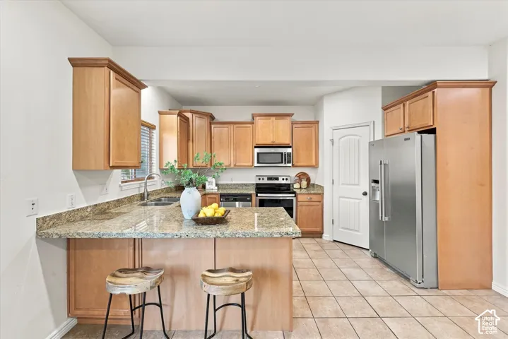 Spacious kitchen featuring wood cabinetry, granite countertops, stainless steel appliances, a breakfast bar, and tile flooring