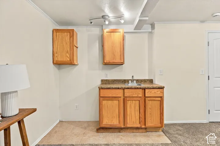 Wet bar with wood cabinetry, speckled countertop, and stainless steel sink