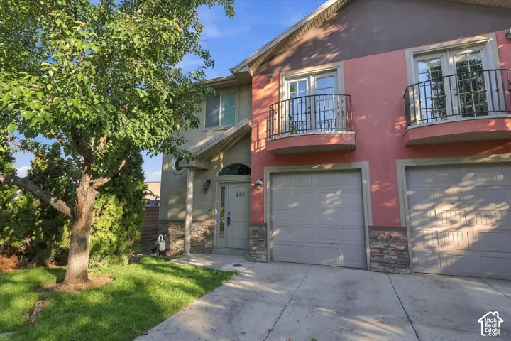 Stucco exterior with stone veneer accents, garage, master-bed balcony, and a concrete driveway