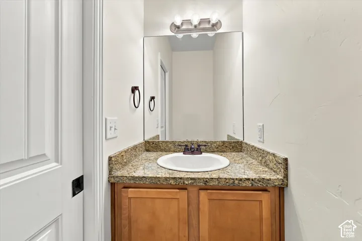 Main level half-bath with light wood-finish vanity with cabinet storage, drop-in sink with bronze-finish faucet, and a wall-mounted mirror