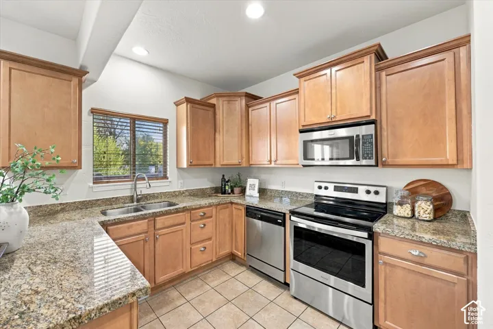 Kitchen featuring wood cabinetry, granite-finish countertops, stainless steel appliances, and tile flooring