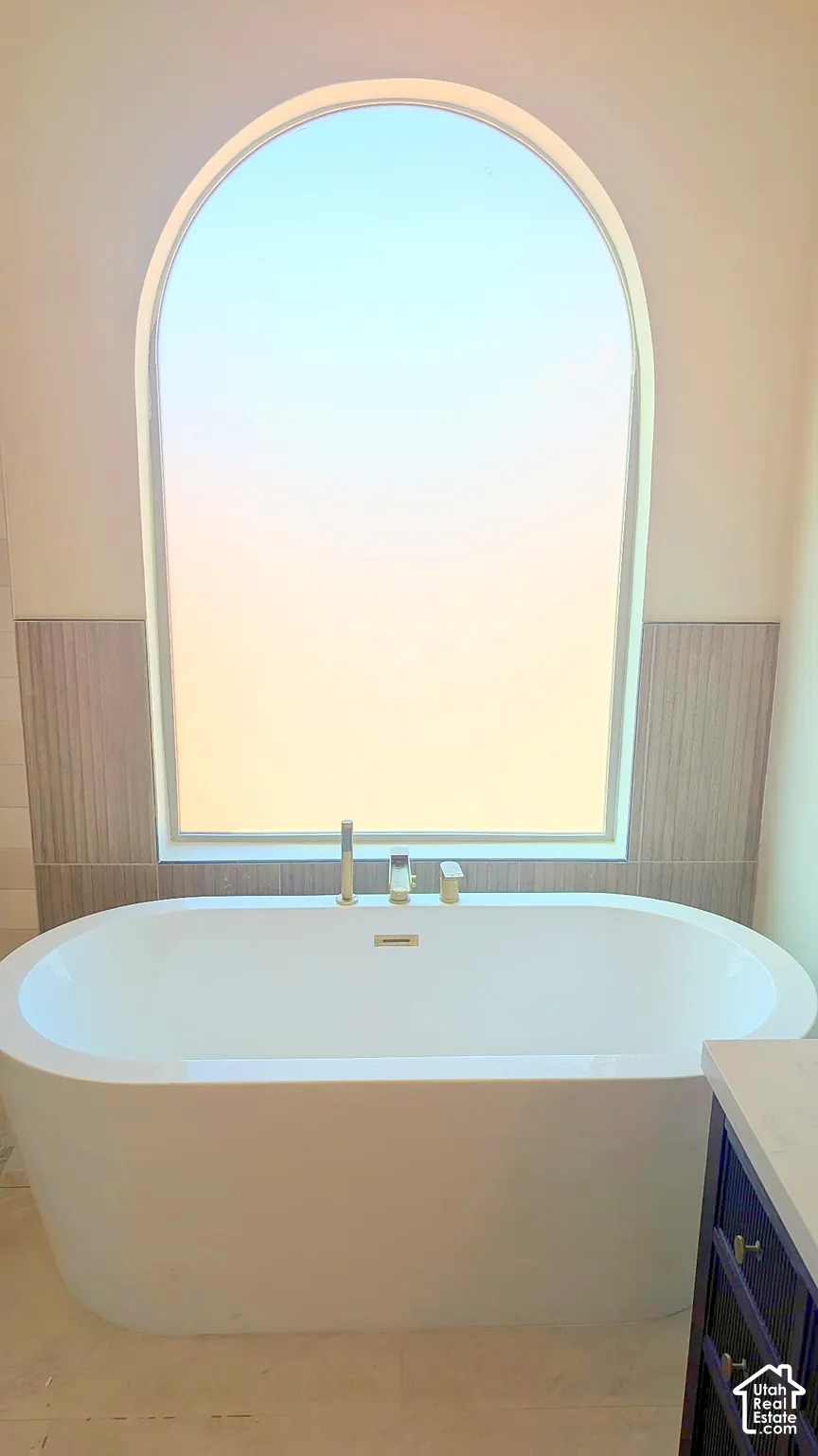 Freestanding soaking tub with a deck-mounted faucet, set beneath an arched window featuring a textured tile surround