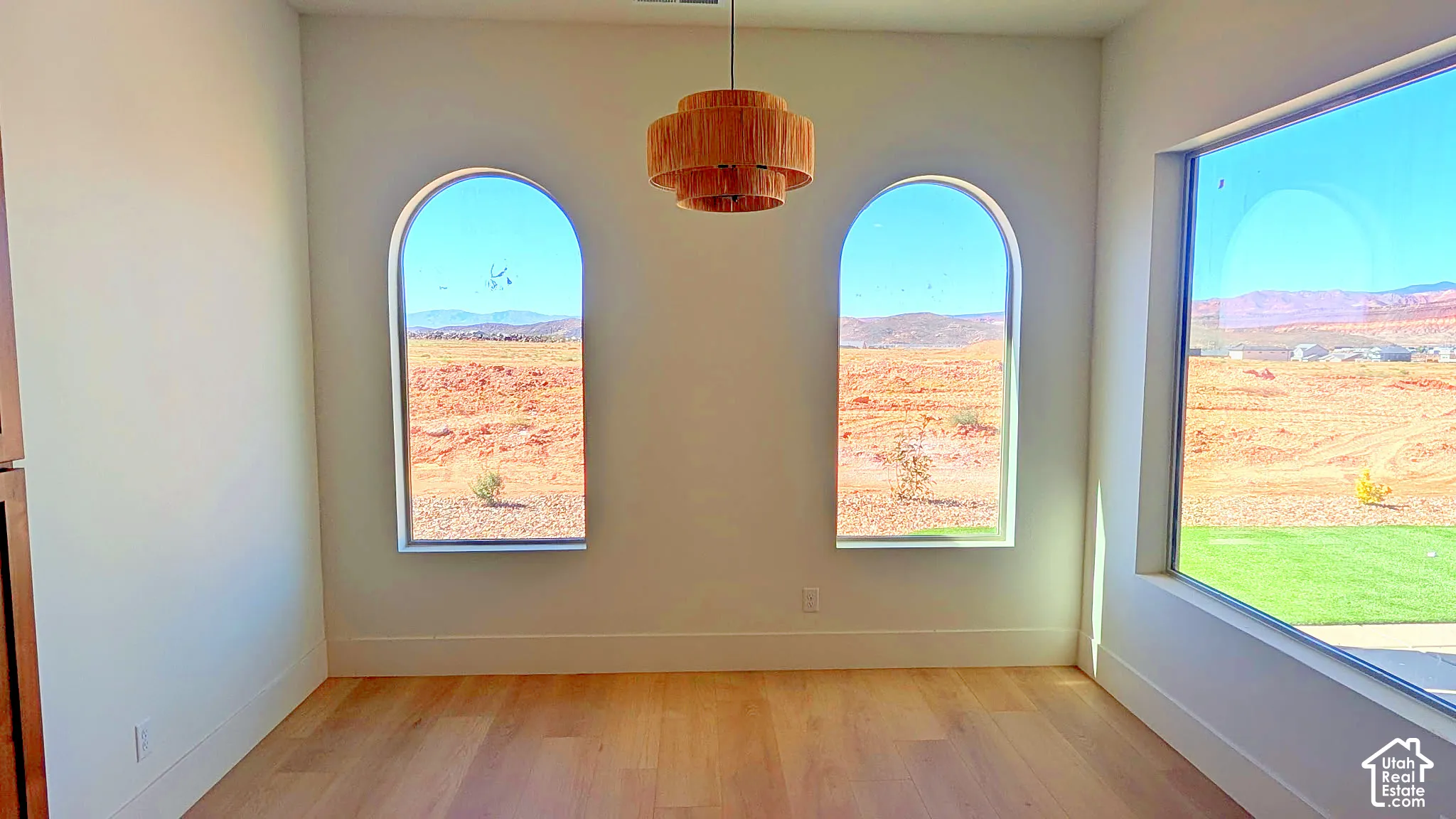 Light-filled room featuring wide-plank wood-finish flooring, two arched windows, a large floor-to-ceiling picture window, and a tiered pendant light fixture