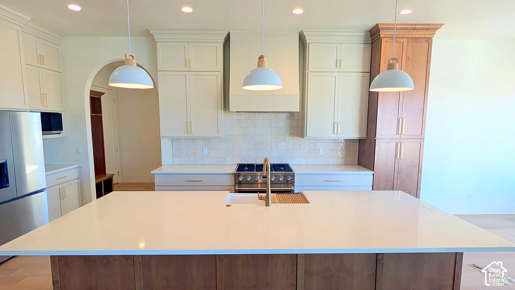 Kitchen featuring an expansive center island with quartz countertops, custom two-tone cabinetry, a professional-style range with a matching range hood, and pendant lighting