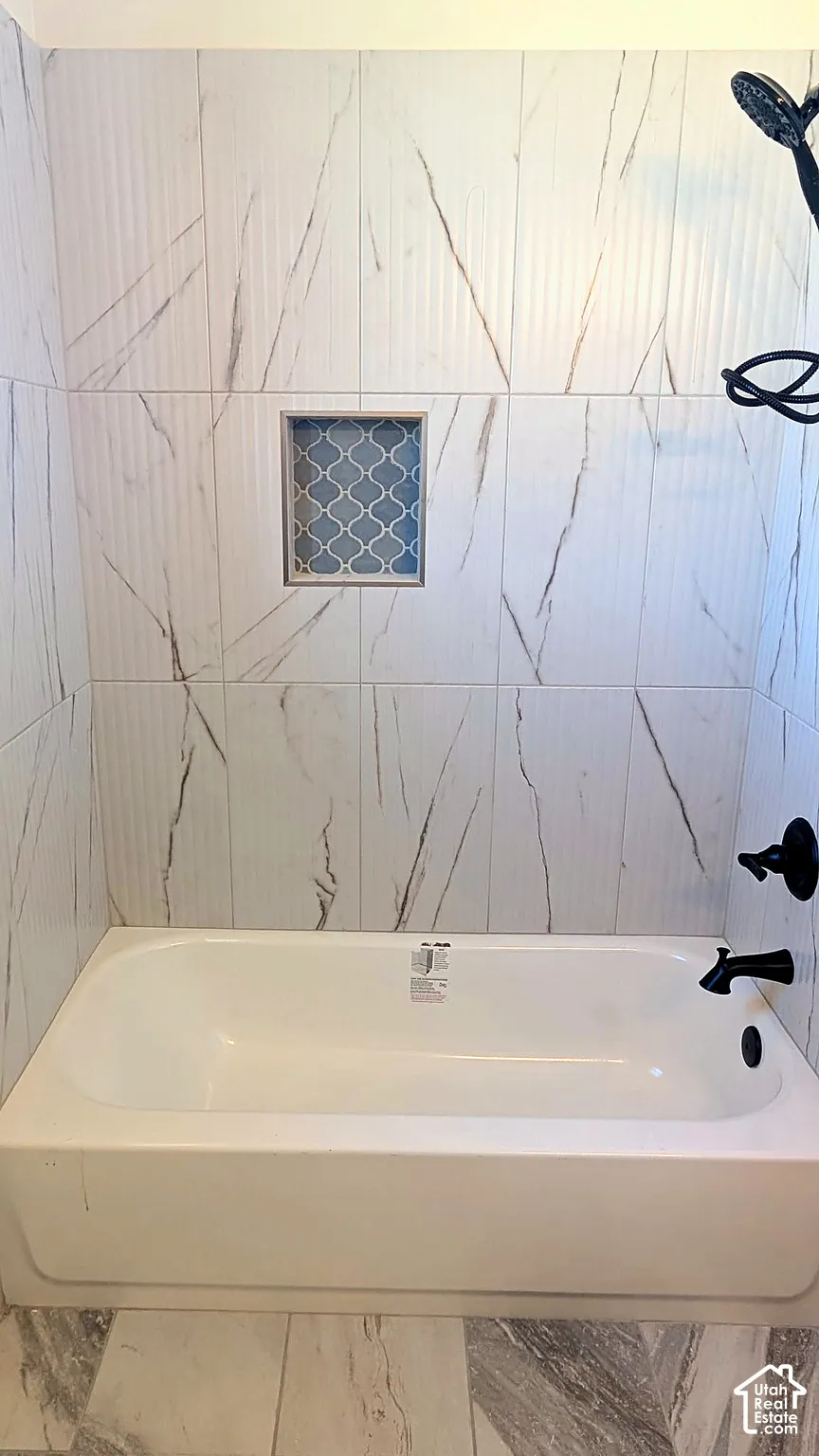 Bathtub with shower head and matte black fixtures, full-height wall tile featuring a patterned inlay niche, and large-format tile flooring