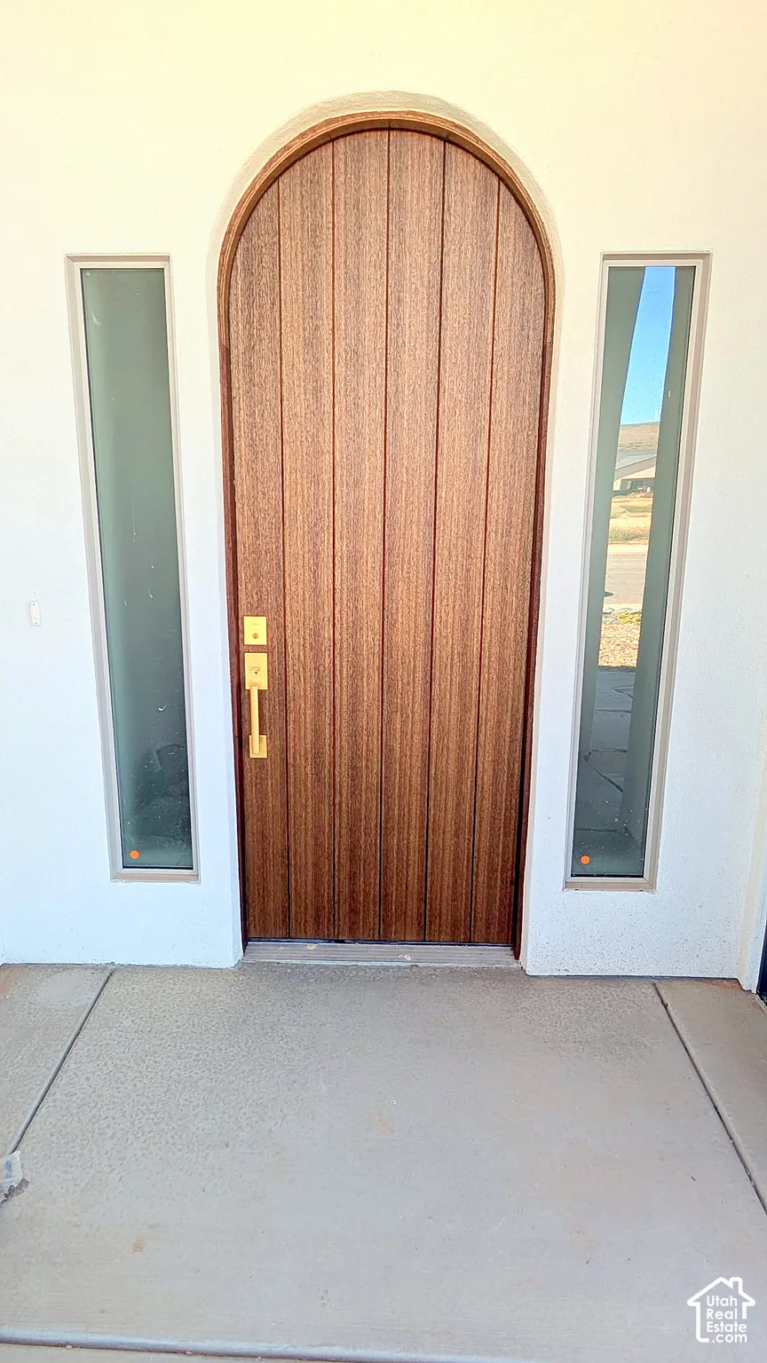 Arched wood-finish entry door featuring vertical paneling, brushed metallic hardware, and dual sidelight windows set into a smooth stucco exterior